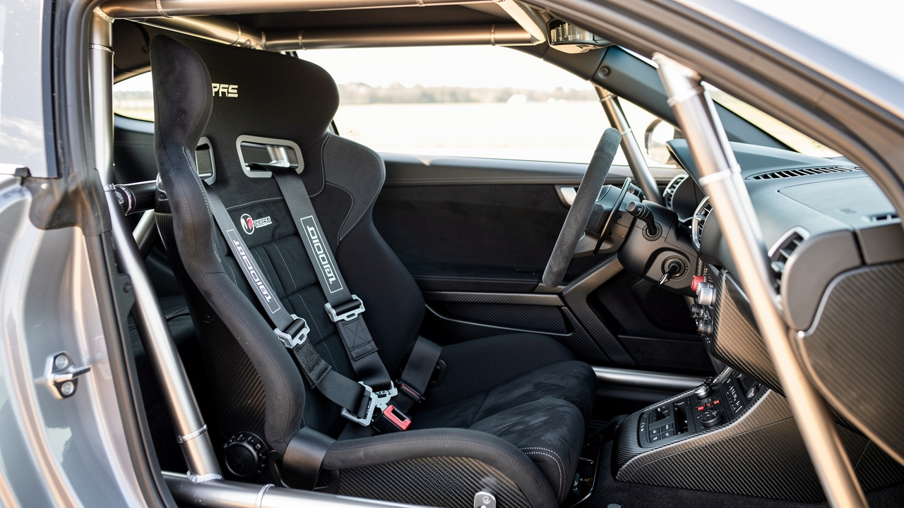 Intérieur technique d’une voiture de course montrant un siège baquet noir, un harnais multipoints, un arceau de sécurité et un système HANS posé sur le siège.