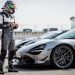 Un pilote amateur portant un casque intégral et une tenue couvrante se tient devant une voiture sportive de série dans le paddock d’un circuit, en pleine journée trackday.